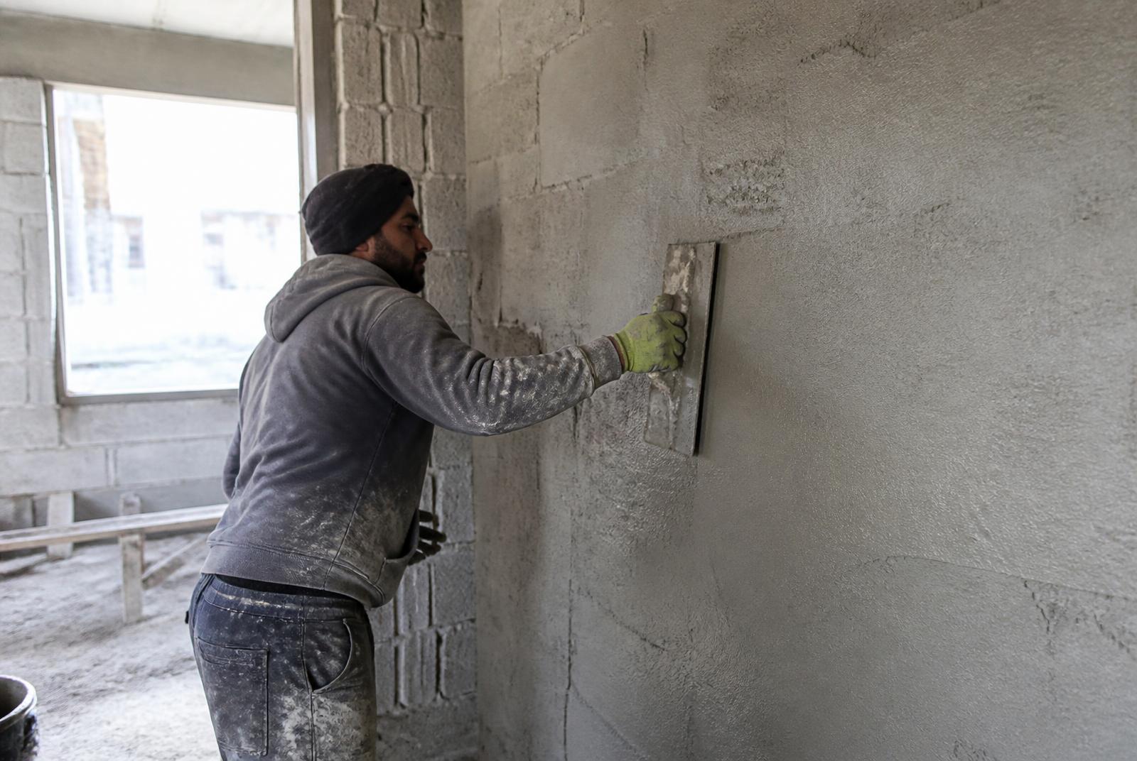 Profissional aplicando revestimento em parede de alvenaria durante etapa de acabamento